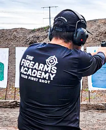 A Firearms Academy instructor in a branded shirt shooting at silhouette targets on an outdoor range in Brownsville, Texas