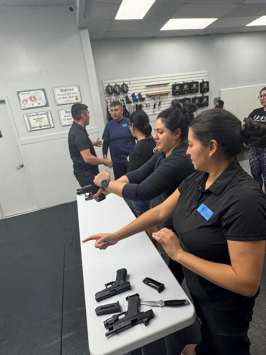 An instructor correcting a student’s grip and stance one-to-one, with training pistols laid out on the table