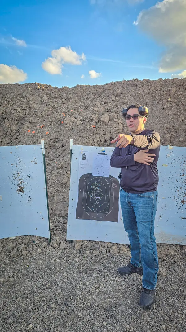 Instructor standing beside an NRA silhouette target on an outdoor range, explaining a shot group to students