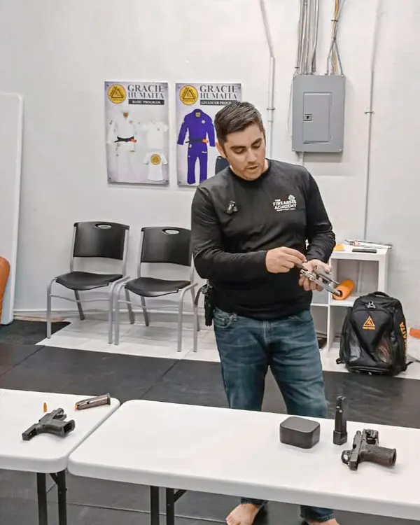 An instructor demonstrating with a training pistol in the Brownsville classroom, with more training pistols laid out on the table