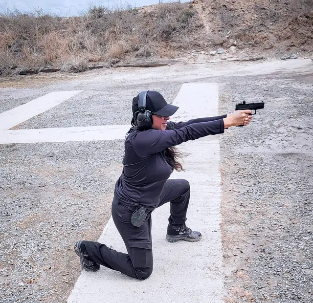 A student shooting from a kneeling position at an outdoor range during defensive pistol training